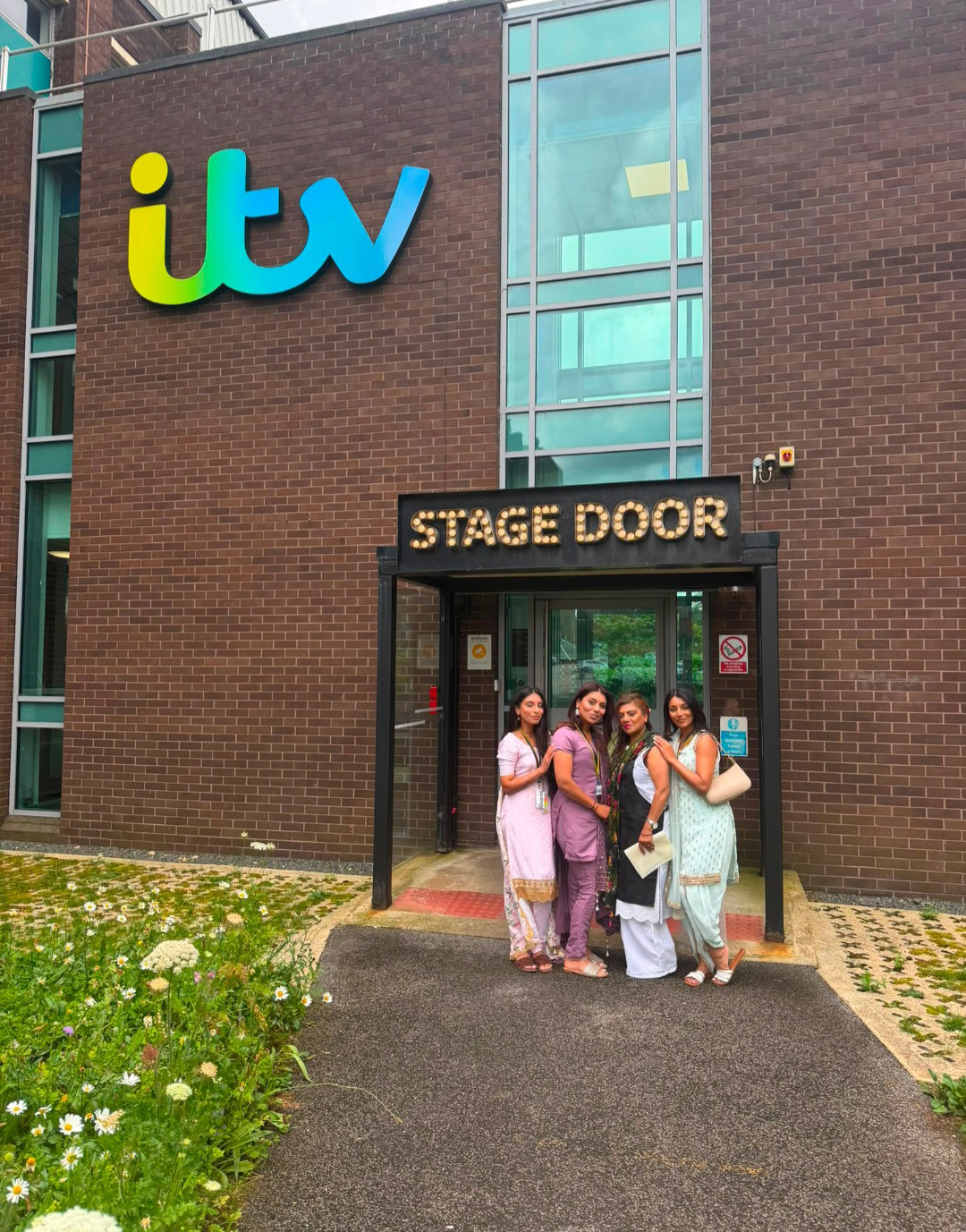 Four people in traditional South Asian outfits standing at the stage door entrance of an ITV building.