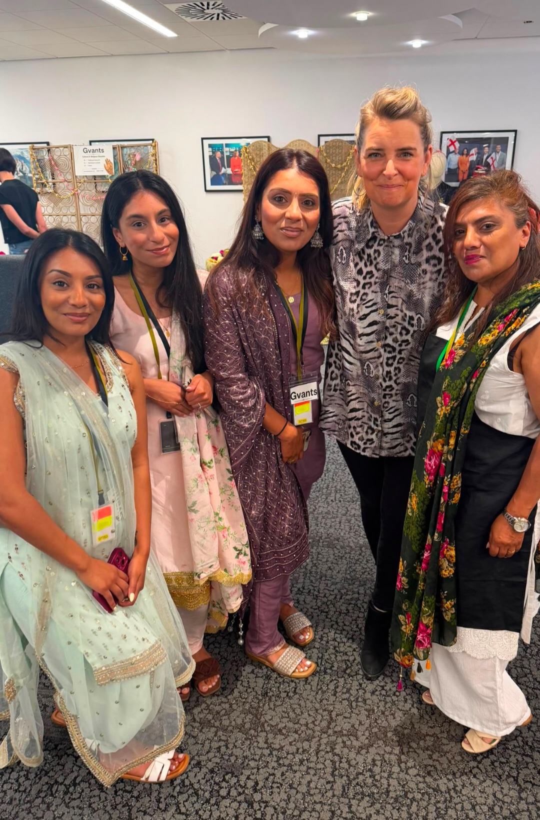 Five people, several wearing traditional South Asian outfits and Gvants passes, standing together at an indoor office event.